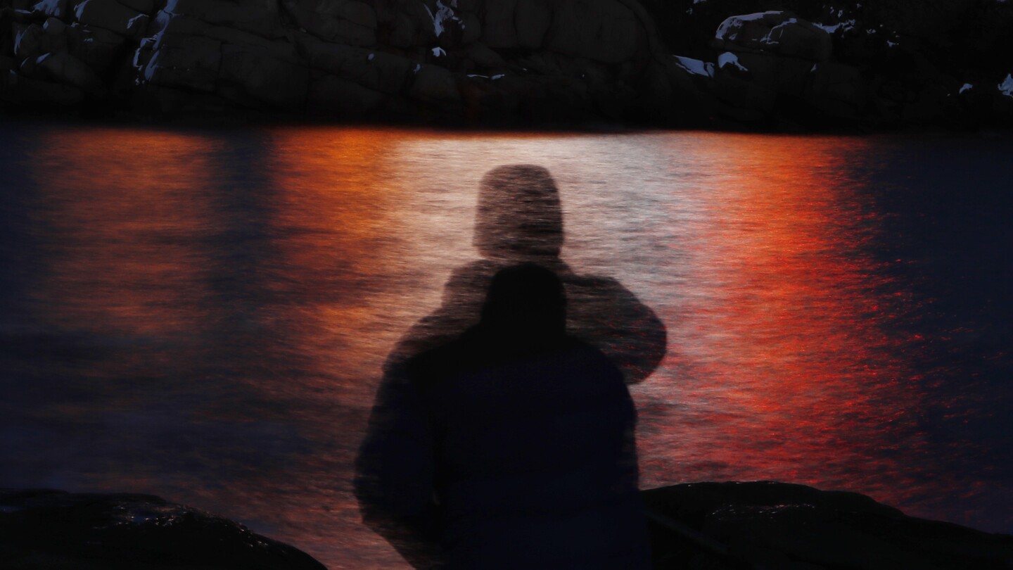 FILE - In this photo made with a long exposure, a man is silhouetted against lights reflected in the waters off Cape Neddick in Maine on Dec. 11, 2017