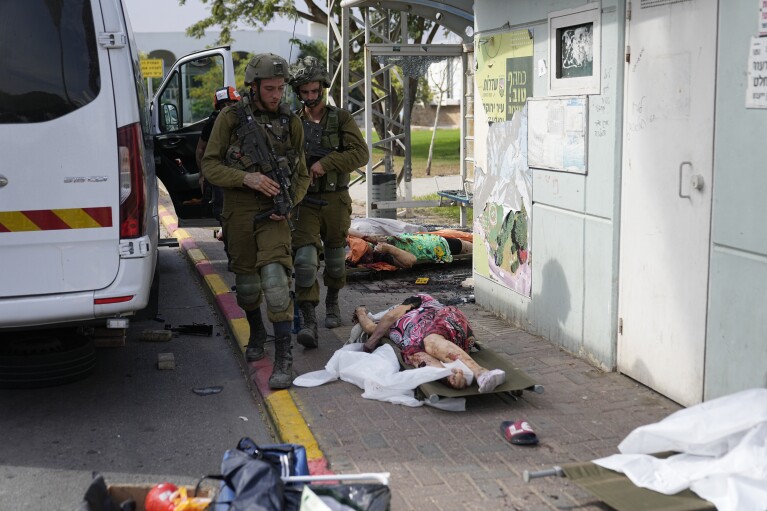 Israeli soldiers walk by civilians killed by Hamas militants in Sderot, Israel, on Saturday, Oct. 7, 2023. (AP Photo/Ohad Zwigenberg)
