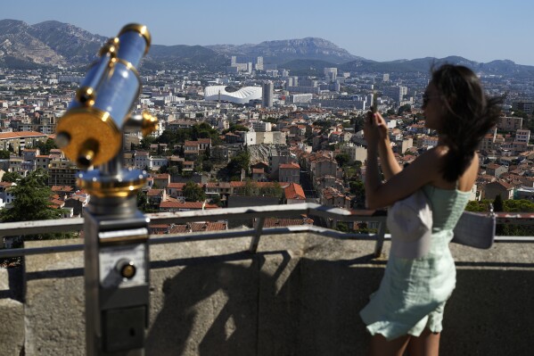 A woman takes a picture from the Notre Dame de la Garde Basilica's viewpoint, with the Velodrome stadium in the background, in Marseille, France, Saturday, Sept. 9, 2023. (AP Photo/Pavel Golovkin)