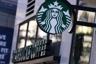 The "Siren" logo hangs outside a Starbucks Coffee shop, Wednesday, July 14, 2021, in Boston. Starbucks said Wednesday, Oct. 27 it is raising its U.S. employees’ pay and making other changes to improve working conditions in its stores.  (AP Photo/Charles Krupa)