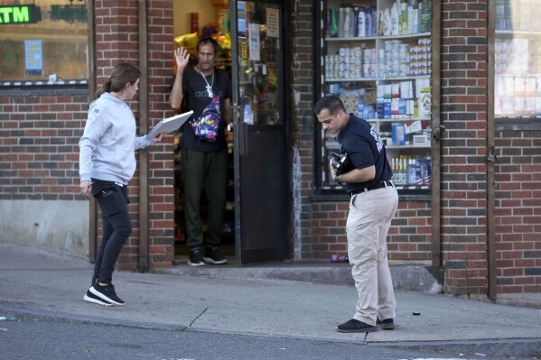 A member of law enforcement, right, investigates a scene where multiple people were shot, Wednesday, Oct. 4, 2023, in Holyoke, Mass. Authorities say the baby of a pregnant woman who was shot Wednesday in Holyoke following a fight on a downtown street was delivered at a hospital and died. (AP Photo/Steven Senne)