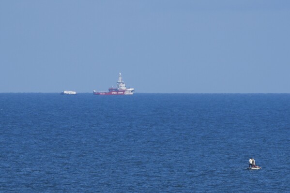 A ship belonging to the Open Arms aid group approaches the shores of Gaza towing a barge with 200 tons of humanitarian aid on Friday, March 15, 2024. (AP Photo/Abdel Kareem Hana)