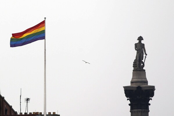 FILE - The rainbow flag, a symbol of the LGBTQ+ community, flies over a building next to Nelson's Column monument, right, in Trafalgar Square, central London, Britain, March 28, 2014. Children who question their gender identity are being let down by lack of evidence and a toxic political debate, according to a report Wednesday from a senior doctor in in England. (AP Photo/Lefteris Pitarakis, File)