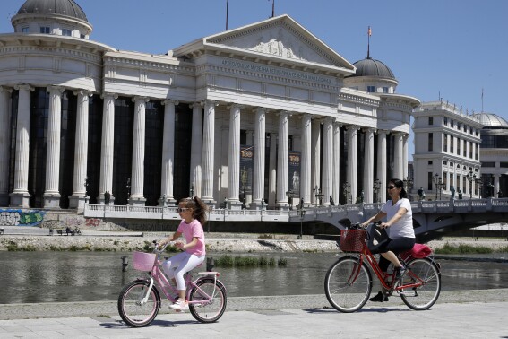 A woman and a girl ride bicycles by Vardar river in downtown Skopje, North Macedonia, on Monday, May 6, 2024. Voters go to the polls on Wednesday in North Macedonia to cast ballots for parliamentary election and presidential runoff, for the second time in two weeks. (AP Photo/Boris Grdanoski)