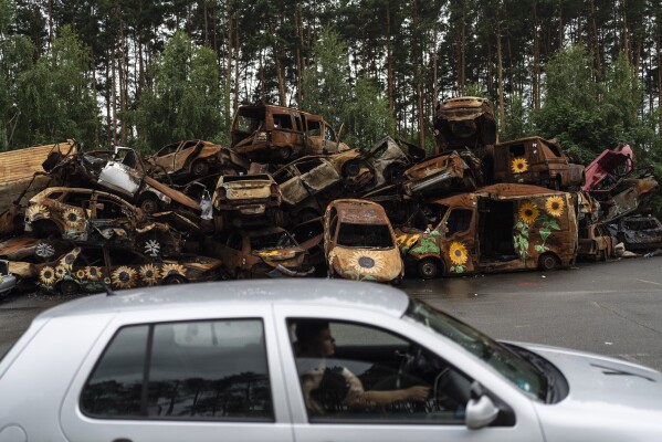 FILE - Vehicles destroyed by Russian attacks are piled up in a lot as a driving instructor, foreground, talks to his student driver in Irpin, Ukraine, Friday, July 7, 2023. (AP Photo/Jae C. Hong, File)