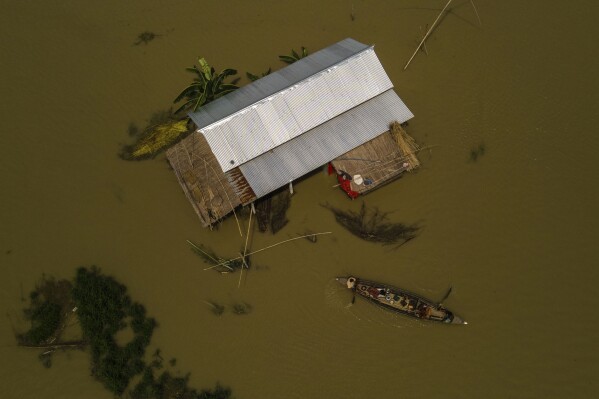 Yaad Ali, 55, left, and his wife Monuwara Begum, 45, center, and Musikur Alam, 14, leave their submerged house on a boat in Sandahkhaiti, a floating island village in the Brahmaputra River in Morigaon district, Assam, India, Wednesday, Aug. 30, 2023. (AP Photo/Anupam Nath)