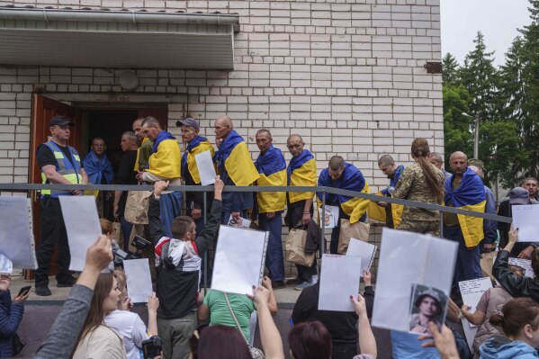 Ukrainian soldiers walk though human corridor with people holding photos of their missed relatives after returning from captivity during a POWs exchange between Russia and Ukraine, in Chernyhiv region, Ukraine, Saturday, May 24, 2025. (AP Photo/Evgeniy Maloletka)