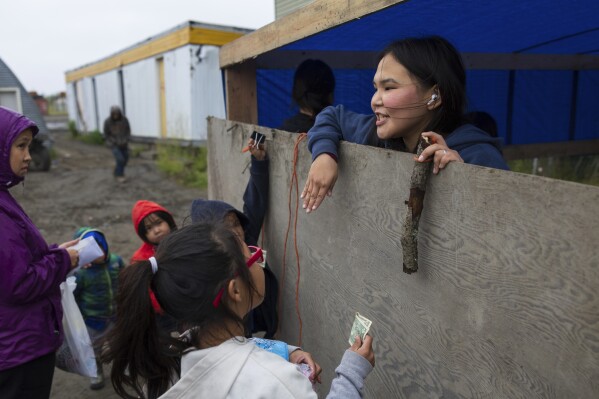 A carnival worker collects money from villagers at a fishing game, Thursday, Aug. 17, 2023, in Akiachak, Alaska. The village hosted a multiday carnival with games and prizes for the village youth. (AP Photo/Tom Brenner)