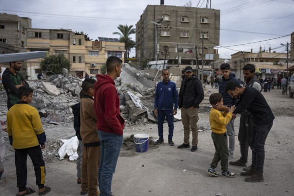 Ibrahim Hassouna, right, the only survivor among his family, stands in front of the ruins of his family home with his friends, in Rafah, southern Gaza Strip, Tuesday, February 13, 2024. On Monday, February 12, Hassouna lost eight people and family members, including three children, say... The house was bombed during an Israeli operation to rescue hostages held in a building in another part of the city.  (AP Photo/Fathima Shabir)