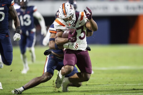 Virginia Tech running back Bhayshul Tuten (33) is tackled by Virginia safety Jonas Sanker, center back, during the second half of an NCAA college football game Saturday, Nov. 25, 2023, in Charlottesville, Va. (AP Photo/Mike Caudill)
