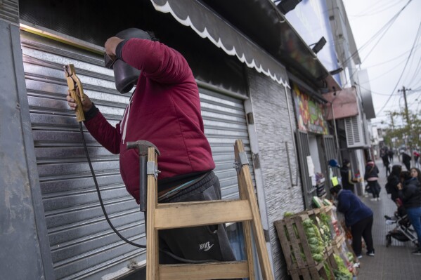 Roger Oscosivi welds a reinforced metal door at the entrance of his supermarket after threats of looting in Loma Hermosa on the outskirts of Buenos Aires, Argentina, Wednesday, Aug 23, 2023. (AP Photo/Victor R. Caivano)