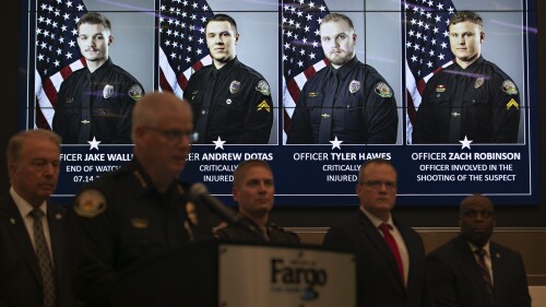 Offizielle Porträts von Polizeibeamten aus Fargo, North Dakota, die einen Tag zuvor an einer Schießerei beteiligt waren, werden während einer Pressekonferenz am Samstag, 15. Juli 2023, im Rathaus von Fargo gezeigt.  Officer Jake Wallin, ganz links, wurde tödlich erschossen.  Die Beamten Andrew Dotas und Tyler Hawes wurden beide lebensgefährlich verletzt.  Auf dem Bild ist auch der Beamte Zachary Robinson zu sehen, der den Verdächtigen getötet hat und sich in bezahltem Verwaltungsurlaub befindet.  Nach Angaben der Behörden wurde auch ein Zivilist verletzt.  (AP Photo/Ann Arbor Miller)