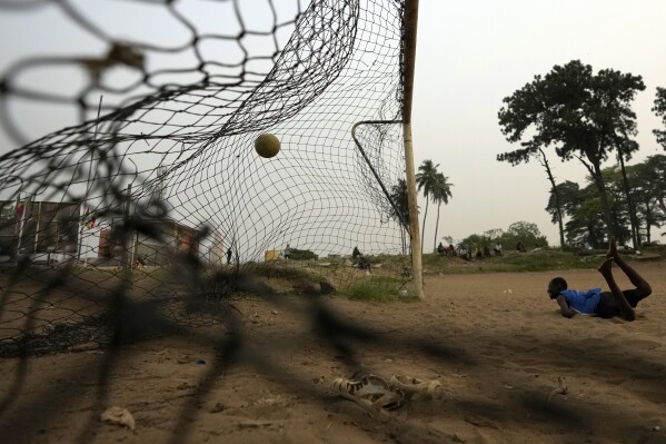 A young man watches the ball after diving while playing football on a dusty field in Abidjan, Ivory Coast, Tuesday, Feb. 6, 2024. (APPhoto/Themba Hadebe)