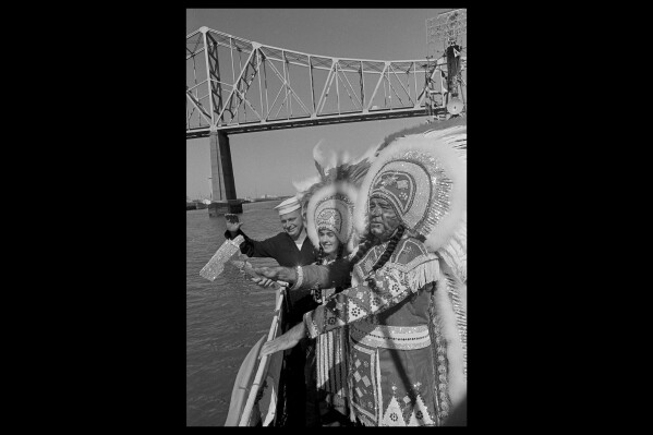 Carnival Chief Choctaw, Stanley L. Sutherland and Princess Pamela Peres wave their tomahawks as they pass under the Mississippi River bridge at New Orleans, Jan. 28, 1967 aboard the Navy Reserve training destroyer USS Hyman. Also getting into the waving act is Seaman Gerald Glatt of Chicago, Ill., who is on two weeks active duty in New Orleans. The Krewe of Choctaw is the first of eleven days of parades before Mardi Gras Day on February 7. (AP Photo/Jack Thornell, file)