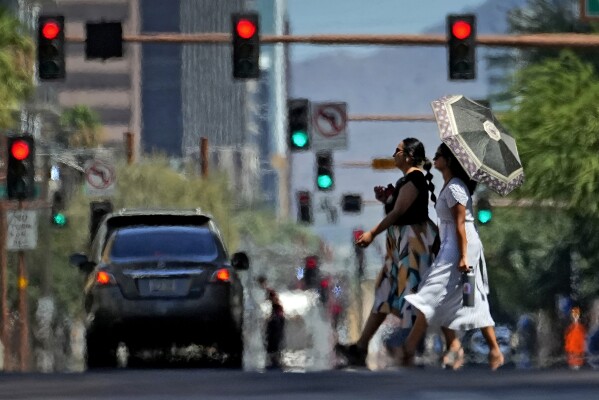 FILE - Heat ripples engulf two ladies while crossing the street on July 17, 2023, in downtown Phoenix. Revved-up climate change now permeates Americans’ daily lives with harm that is “already far-reaching and worsening across every region of the United States," a massive new government report says Tuesday, Nov. 14. (AP Photo/Matt York, File)