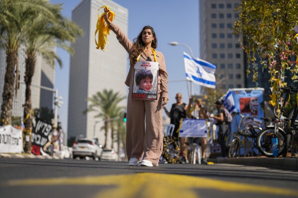 A woman, with a photograph of a child who was abducted during the unprecedented Hamas attack on Israel, hands out yellow ribbons to passing drivers in central Tel Aviv, Israel, Wednesday, Oct. 25, 2023. Yellow ribbons is the symbol for those who are actively asking for the release of Israeli hostages held by Hamas in Gaza. (AP Photo/Francisco Seco)