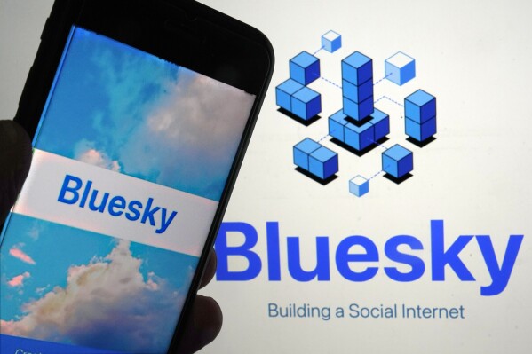 FILE - The app for Bluesky is shown on a mobile phone, left, and on a laptop screen, Friday, June 2, 2023, in New York. Bluesky, a Twitter-like social network championed by Twitter co-founder Jack Dorsey, has emerged from its cocoon and is now allowing anyone to create an account and join the service. Until Tuesday, Feb. 6, 2024, users needed an invitation to join the network, which typically meant hunting down an existing member and begging for an invite. That gave the site time to build out moderation tools and other features, it said. (AP Photo/Richard Drew, File)