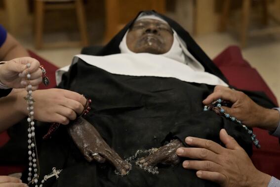 People pray over the body of Sister Wilhelmina Lancaster at the Benedictines of Mary, Queen of Apostles abbey Sunday, May 28, 2023, near Gower, Mo. Hundreds of people visited the small town in Missouri this week to see the nun's body that has barely decomposed since 2019 — some are saying it's a sign of holiness in Catholicism, while others are saying the lack of decomposition may not be as rare as people think. (AP Photo/Charlie Riedel)
