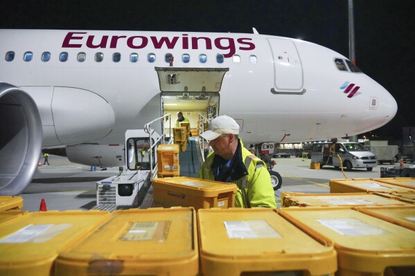 WISAG employees load a Eurowings Airbus A320-214 bound for Stuttgart with plastic boxes full of mail, at Berlin Brandenburg Airport, in Schönefeld, Germany, Thursday, March 28, 2024. Germany's main national postal carrier on Thursday put an end to domestic flights to transport letters, stopping the practice after nearly 63 years in a move that will allow it to improve its climate footprint and reflects the declining significance of letter mail. Deutsche Post said the last planes carrying letters between northern and southern Germany, operated by Lufthansa unit Eurowings and Tui Fly, flew overnight on the Stuttgart-Berlin, Hannover-Munich and Hannover-Stuttgart routes. (Soeren Stache/dpa via AP)