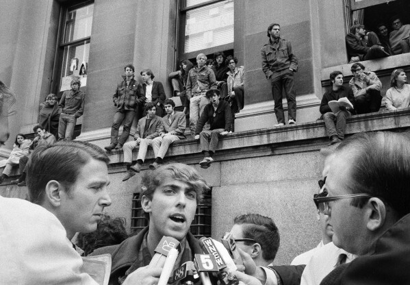 FILE - Mark Rudd, a leader of the student protest at Columbia University in New York City, is interviewed outside Low Memorial Library, background, April 25, 1968, which has been occupied by students since the previous day. Rudd said the purpose of the protest was to "hit at" what he claimed was the university's policy of "racism and support for imperialism." (AP Photo/File)