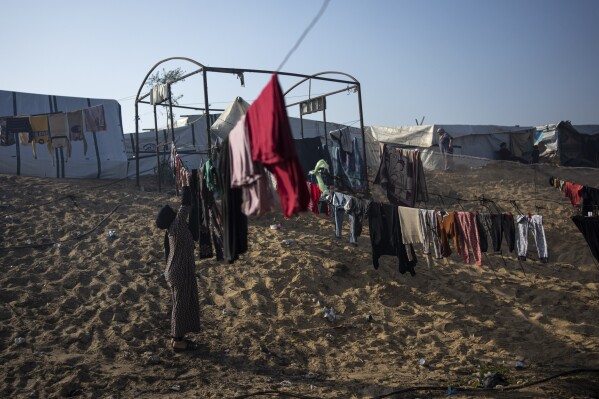 Majida Abu Jarad, who was displaced by the Israeli bombardment of the Gaza Strip, collects the laundry at a makeshift tent camp in the Muwasi area, southern Gaza, Monday, Jan. 1, 2024. (AP Photo/Fatima Shbair)