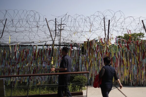 Visitors look on the wire fence decorated with ribbons written with messages wishing for the reunification of the two Koreas at the Imjingak Pavilion in Paju, South Korea, Tuesday, June 9, 2020. North Korea said Tuesday it will cut off all communication channels with South Korea as it escalates its pressure on the South for failing to stop activists from floating anti-Pyongyang leaflets across their tense border. (AP Photo/Lee Jin-man)