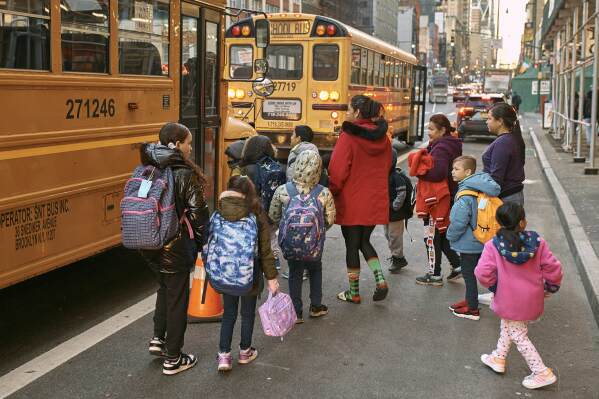 Migrant children prepare to board a school bus while guided by their guardians in front of the Row Hotel that serves as migrant shelter on Tuesday, Dec. 12, 2023, in New York. (AP Photo/Andres Kudacki)