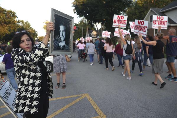 FILE - Felicia Miceli  holds a photograph of her son, Louie Miceli as opponents of a Haymarket drug treatment march toward Peacock Junior High prior to a public hearing on the subject on Wednesday, Sept. 18, 2019 in Itasca, Ill.  Haymarket Center, a Chicago-based addiction treatment center, which like others nationwide has faced fierce opposition to opening suburban branches, filed a federal lawsuit Tuesday, Jan. 11, 2022, to force one suburb, Itasca,  to stop blocking its expansion plans. Miceli's son, Louie died of a heroin overdose at the age of 24 in 2012. (Chris Sweda/Chicago Tribune via AP)