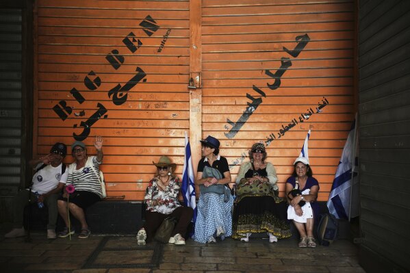 Israelis sit next to a closed Palestinian shop during a march marking Jerusalem Day, an Israeli holiday celebrating the capture of east Jerusalem in the 1967 Mideast war, in Jerusalem's Old City, Monday, May 26, 2025. (AP Photo/Ohad Zwigenberg)