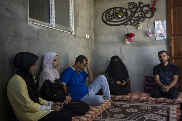 The Zorob family sits inside their one-room hut, covered in nylon sheets in Khan Younis, southern Gaza Strip, Monday, Aug. 28, 2023. The Gaza Strip's displaced families await the completion of nearly 1,400 Egyptian-sponsored housing units, a project mired in political disputes between the Palestinian Authority and Gaza's Hamas-run government. The Zorob family, like thousands of others, remains caught in the crossfire, living in makeshift conditions while nearly completed apartments stand empty.(AP Photo/Fatima Shbair)