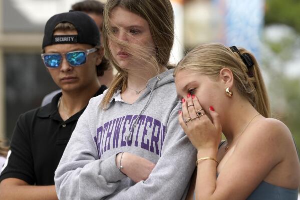Helena Kavanaugh, right, stands with friends Addison Schwan, center, and Charlie Shookman after Kavanaugh placed flowers at a memorial for the seven people who lost their lives in the Highland Park, Ill., Fourth of July mass shooting, Wednesday, July 6, 2022, in Highland Park. (AP Photo/Charles Rex Arbogast)