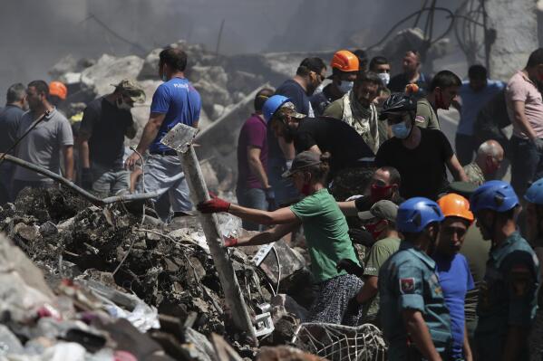 Armenian emergency employees and volunteers work on the side of burned Surmalu market about two kilometers (1.2 miles) south of the center of Yerevan, Armenia, Monday, Aug. 15, 2022. Armenian officials say that the death toll in a fireworks storage explosion in the country's capital has risen to six. A powerful blast tore through a fireworks depot at a popular market in Armenia's capital on Sunday, setting off a massive fire that sent a towering column of thick smoke over the center of Yerevan. (Vahram Baghdasaryan/Photolure via AP)