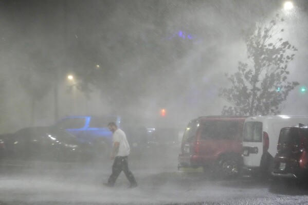 FILE - Max Watts, of Buford, Ga., walks in the parking lot to check on a trailer parked outside the hotel where he is riding out Hurricane Milton with coworkers, Wednesday, Oct. 9, 2024, in Tampa, Fla. Watts, who works for a towing company, was deployed with colleagues to Florida to aid in the aftermath of the storm. (AP Photo/Julio Cortez, File)