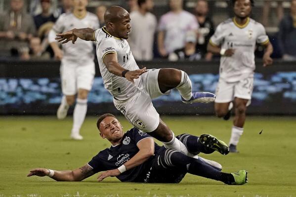 Sporting Kansas City defender Kortne Ford, bottom, and Columbus Crew midfielder Darlington Nagbe get tangled up while chasing the ball during the first half of an MLS soccer match Saturday, April 23, 2022, in Kansas City, Kan. (AP Photo/Charlie Riedel)
