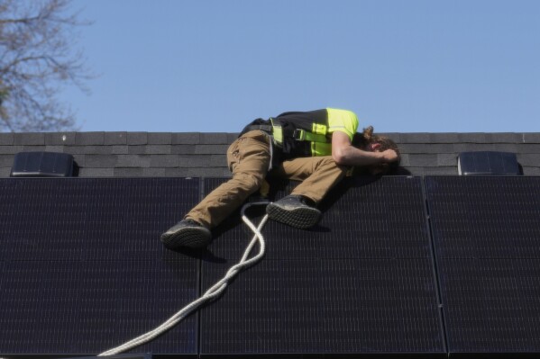 Theodore Tanczuk, of solar installer YellowLite, puts a panel on the roof of a home in Lakewood, Ohio, Wednesday, April 16, 2025. (AP Photo/Sue Ogrocki)