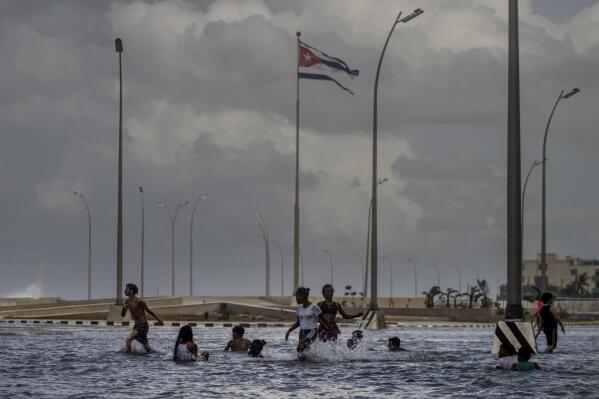 FILE - A Cuban flag, shredded by the winds of Hurricane Ian, flies in the air while children play in the seawater from the waves breaking on Malecon in Havana, Cuba, Thursday, Sept. 29, 2022. Eighteen former Latin American and Caribbean leaders have signed a letter to U.S. President Joe Biden to be released Wednesday, Nov. 2, 2022, asking the United States to remove its six-decade embargo on Cuba in the wake of devastating damage inflicted by Hurricane Ian. (AP Photo/Ramon Espinosa, File)