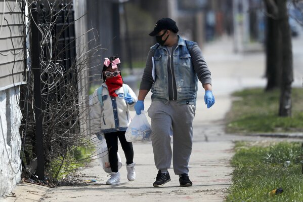 In this April 7, 2020, photo, Erica Harris, right, and her daughter Jordan, wear their protective masks as they walk back home after getting a lunch and homework from the child’s school on Chicago’s Southside in Chicago. As the coronavirus tightened its grip across the country, it is cutting a particularly devastating swath through an already vulnerable population, black Americans. (AP Photo/Charles Rex Arbogast)