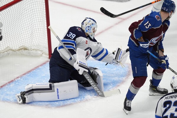 Winnipeg Jets goaltender Laurent Brossoit, left, makes a glove-save of a redirected shot by Colorado Avalanche right wing Valeri Nichushkin (13) in the third period of Game 4 of an NHL Stanley Cup first-round playoff series Sunday, April 28, 2024, in Denver. (AP Photo/David Zalubowski)