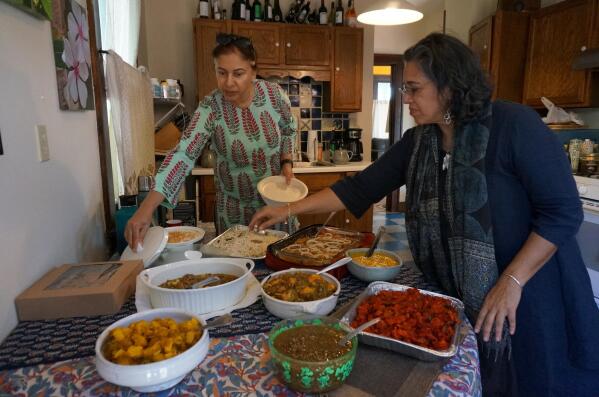 Kuljeet Kaur, left, helps arrange a potluck lunch of Indian dishes in the kitchen of Meena Natarajan in Minneapolis on Sunday, Oct. 9, 2022. Kaur, who’s Sikh, and Natarajan, who comes from a Hindu family, gather monthly with other Indians in Minnesota in an interfaith group aimed to prevent religious tensions in India from spilling over into US diaspora communities. (AP Photo/Giovanna Dell’Orto)