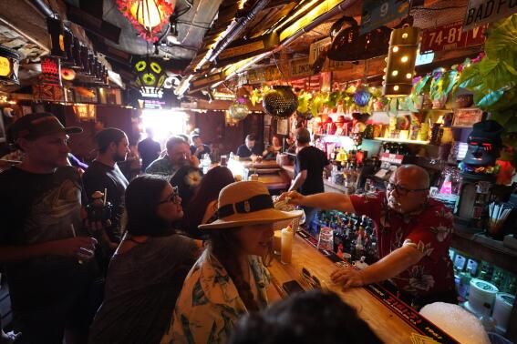 FILE - In this Wednesday, July 7, 2021, file photo, patrons enjoy tropical cocktails in the tiny interior of the Tiki-Ti bar as it reopens on Sunset Boulevard in Los Angeles. Public health officials in Los Angeles County will begin requiring proof of COVID-19 vaccination for patrons and workers at indoor bars, wineries, breweries and nightclubs next month. The new initiative in the nation’s most populous county begins Oct. 7, 2021 with proof of at least one vaccine dose required. (AP Photo/Damian Dovarganes, File)