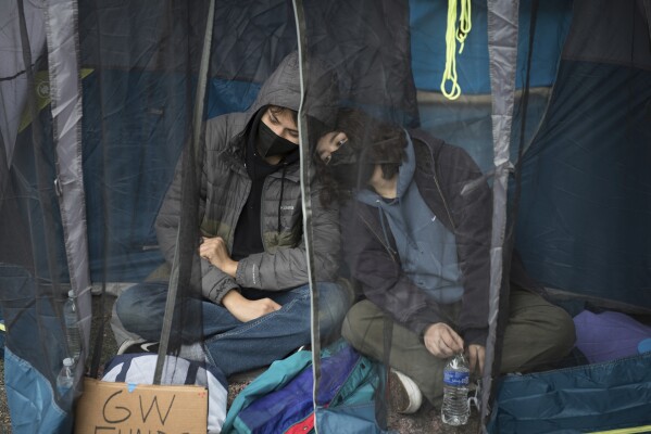 Students protesting the Israel-Hamas war at George Washington University sit in a tent to avoid the rain in Washington, Saturday, April 27, 2024. Protests and encampments have sprung up on college and university campuses across the country to protest the war. (AP Photo/Cliff Owen)