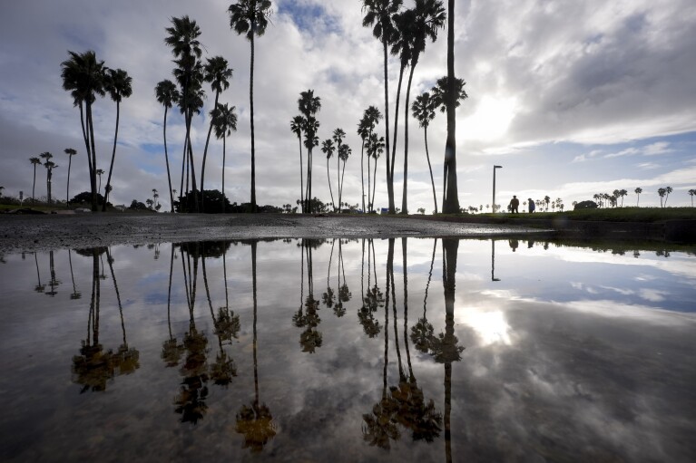 FILE - Two people walk along Mission Bay during a break in the rain on Feb. 1, 2024, in San Diego. California's current rainy season got off to a slow start but has rebounded with recent storms that have covered mountains in snow and unleashed downpours, flooding and mudslides. The water content of the vital Sierra Nevada snowpack has topped 80% of normal to date while downtown Los Angeles has already received more than an entire year's average annual rainfall. (AP Photo/Gregory Bull, File)