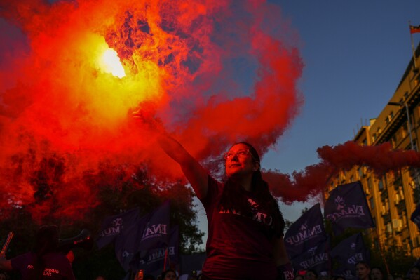 A woman holds a bengala in front of La Moneda presidential palace during an International Women's Day march, in Santiago, Chile Friday, March 8, 2024. (AP Photo/Esteban Felix)