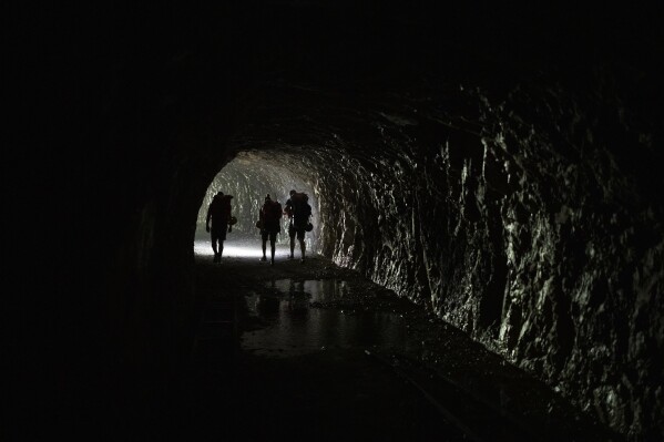 Tourists guided by Antoine Coudray of Secret River Tours hike through a tunnel with packrafts on their backs in the Verdon Gorge, southern France, Monday, June 19, 2023. 