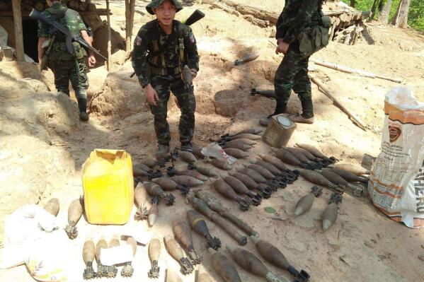 In this photo provided by Karen National Liberation Army, a Karen National Liberation Army soldier holds a motor shell while standing next to a cache of mortar shells found at a Myanmar military outpost Friday, May 7, 2021, in Mutraw district, Karen State, Myanmar. Ethnic Karen guerrillas burned down a Myanmar military outpost Friday morning, capturing it without a fight after its garrison fled at their approach, a senior Karen officer said. (Karen National Liberation Army via AP)