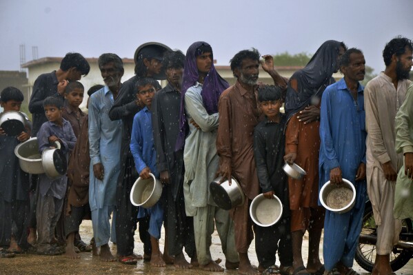 People wait in the rain for their turn to receive free food distributed by volunteers outside a camp of internally displaced people from coastal areas in Sujawal, Pakistan's southern district in the Sindh province, Thursday, June 15, 2023, as Cyclone Biparjoy was approaching. A vast swath of western India and neighboring southern Pakistan that suffered deadly floods last year are bracing for a new deluge as fast-approaching Cyclone Biparjoy whirls toward landfall Thursday. (AP Photo/Pervez Masih)