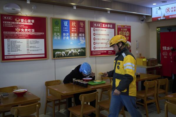 Luo Shuai, right, a food delivery rider for Meituan walks by Liu Lijie, rider from Ele.me as they eat their meals at Yushiji restaurant serving the “aixincan” or “loving meals," in Beijing on March 18, 2025. (AP Photo/Andy Wong)