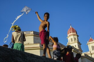 A youth flies a kite outside the shrine of the Virgin of Charity of Cobre in El Cobre, Cuba, on Saturday, Feb. 10, 2024. The Vatican-recognized Virgin, venerated by Catholics and followers of Afro-Cuban Santeria traditions, is at the heart of Cuban identity, uniting compatriots from the Communist-run Caribbean island to those who were exiled or emigrated to the U.S. (AP Photo/Ramon Espinosa)