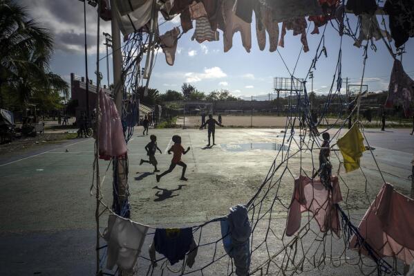 Children run past a goal post used to hang clothes at the Hugo Chavez public square transformed into a refuge for families forced to leave their homes due to clashes between armed gangs in Port-au-Prince, Haiti, Thursday, Oct. 20, 2022. (AP Photo/Ramon Espinosa)