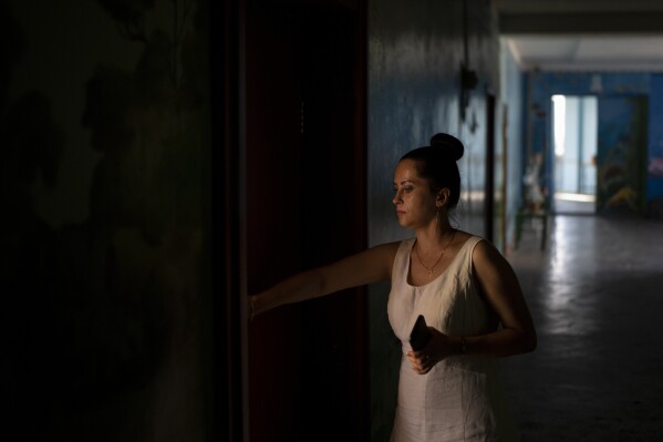 Katarina Chesta opens a door at her work in Kupiansk, Ukraine, Wednesday, Aug. 23, 2023. Chesta says she's staying because she is tired of packing up and running away from war, despite intensified offensive operations by Russian forces in recent weeks. (AP Photo/Bram Janssen)